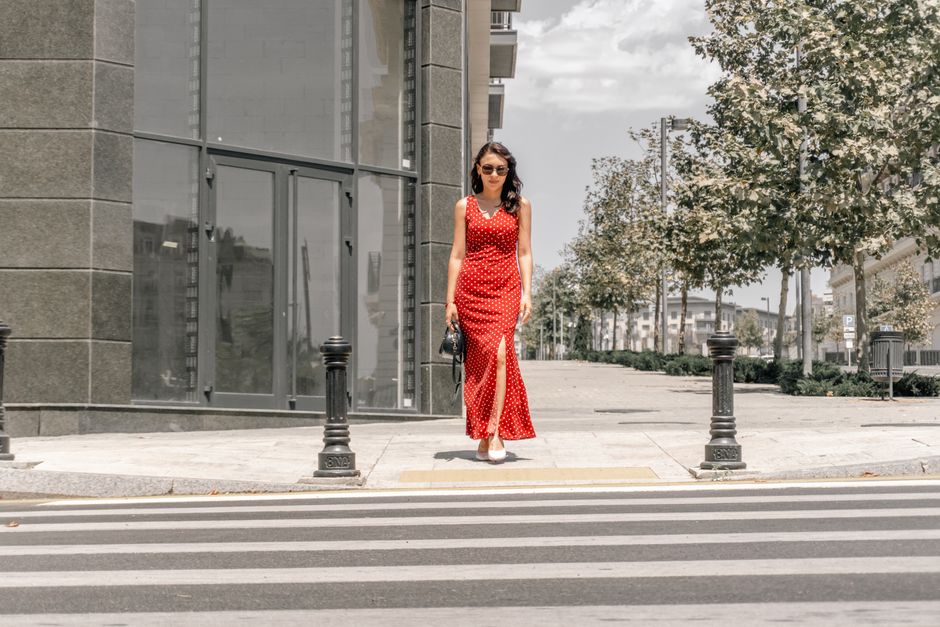 Stylish woman in red dress crosses street in Baku, capturing urban elegance.