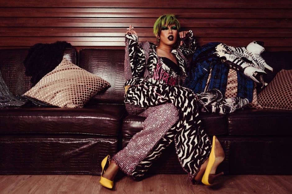 Full length of eccentric transsexual with stylish haircut in trendy clothes relaxing on sofa with cigarette and talking on smartphone