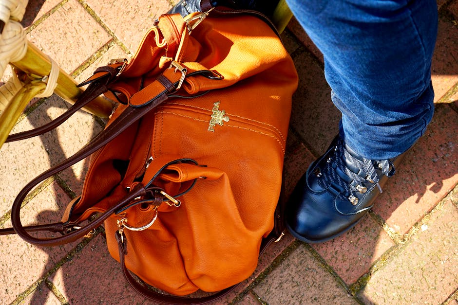 Orange leather bag paired with stylish footwear on sunny brick pavement.