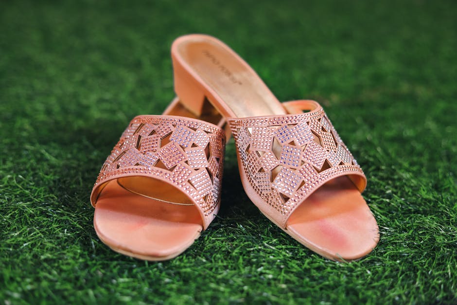 Stylish pink slip-on sandals with intricate designs placed on lush green grass, showcasing fashion elegance.