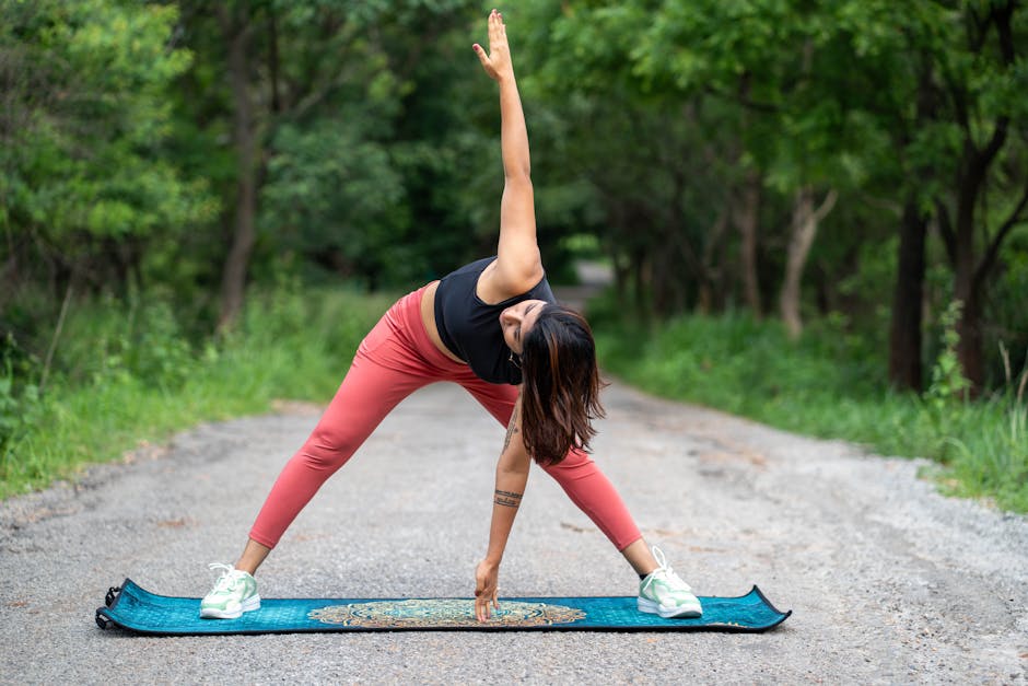 A woman performs yoga on a mat outdoors, surrounded by lush greenery, wearing pink pants.
