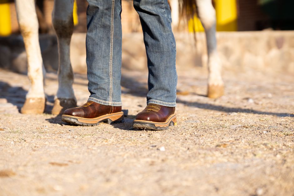 Detailed view of boots and jeans next to a horse on a sunny day, showcasing outdoor rural lifestyle.