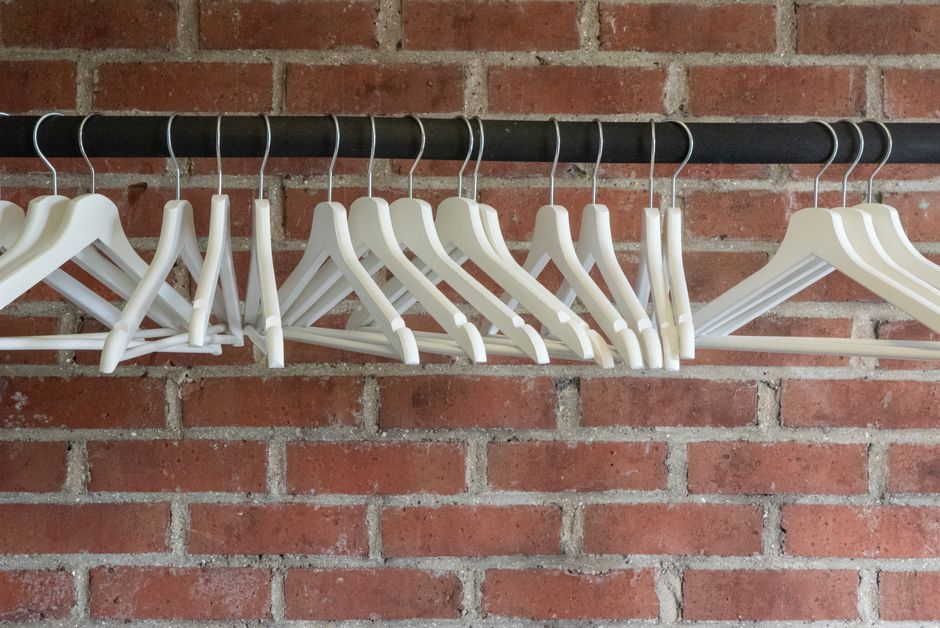 Row of empty white hangers on a black rod set against a red brick wall.