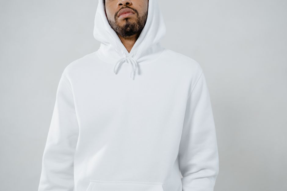 A close-up portrait featuring a man wearing a white hoodie against a light backdrop.