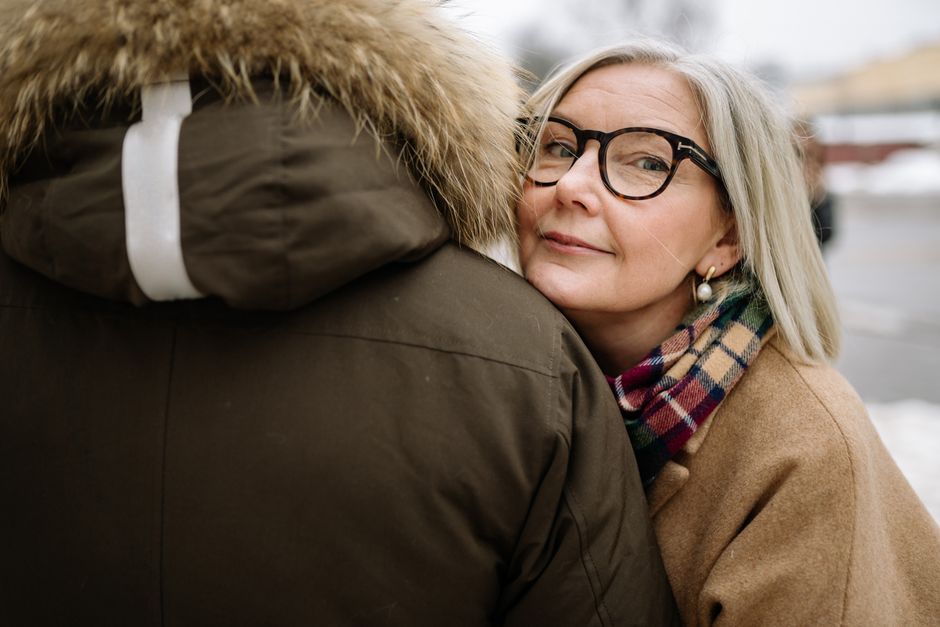 A senior woman wearing eyeglasses embraces a partner outdoors, showcasing warmth and affection in winter attire.