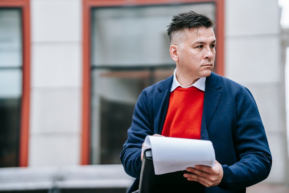 A serious man holding papers, dressed professionally in an urban environment.
