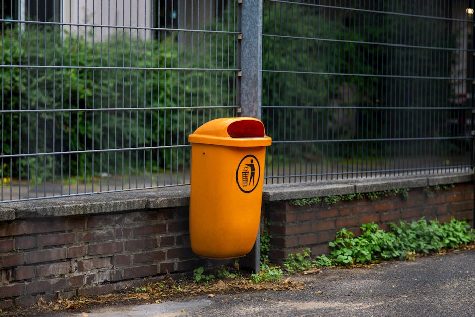 An orange trash bin attached to a brick wall and metal fence, adding contrast to the urban scene.