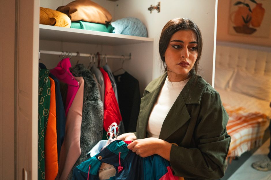 Woman organizing clothes in a closet with thoughtful expression in a modern bedroom.