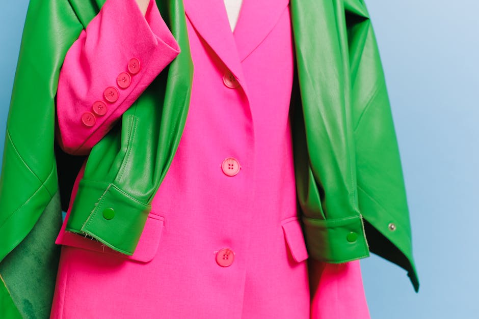 Stylish pink blazer with a contrasting green leather jacket draped over it, showcasing bold fashion colors.