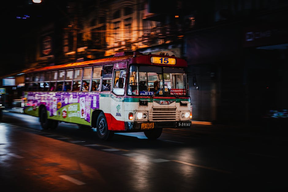 Nighttime street scene with a colorful bus in motion in Bangkok, showcasing urban life.