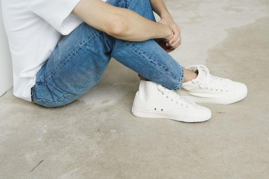 A person in jeans, a white t-shirt, and sneakers sits on a concrete floor indoors.