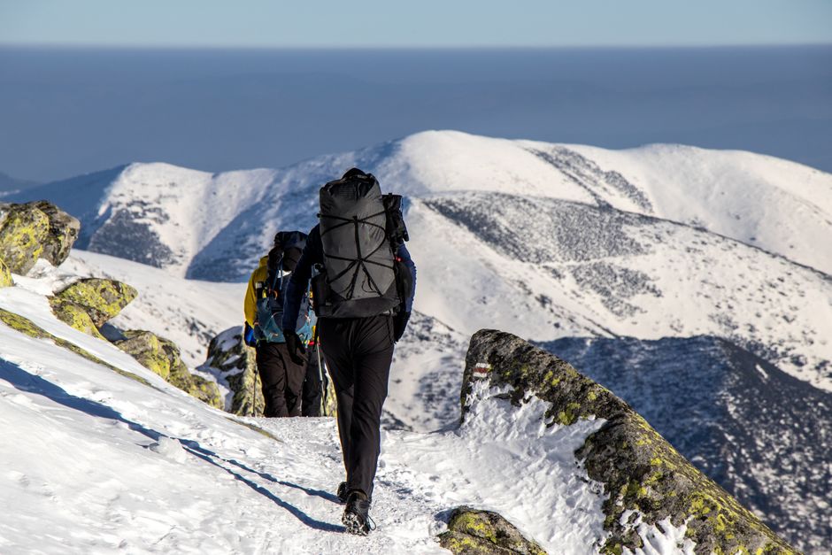 Hikers with backpacks trek through snow-covered mountains on a sunny winter day.